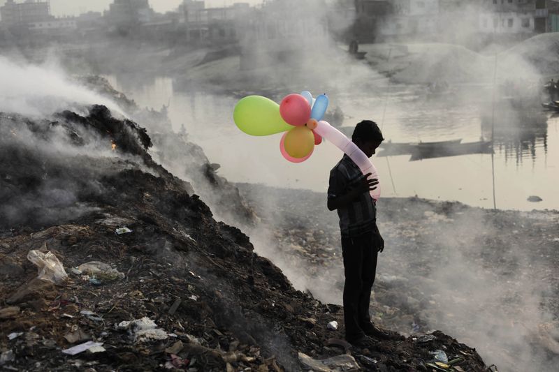 &copy; Reuters. A boy plays with balloons by Buriganga river as smoke emits from a dump yard during sunset in Dhaka January 19, 2013. REUTERS/Andrew Biraj/Files