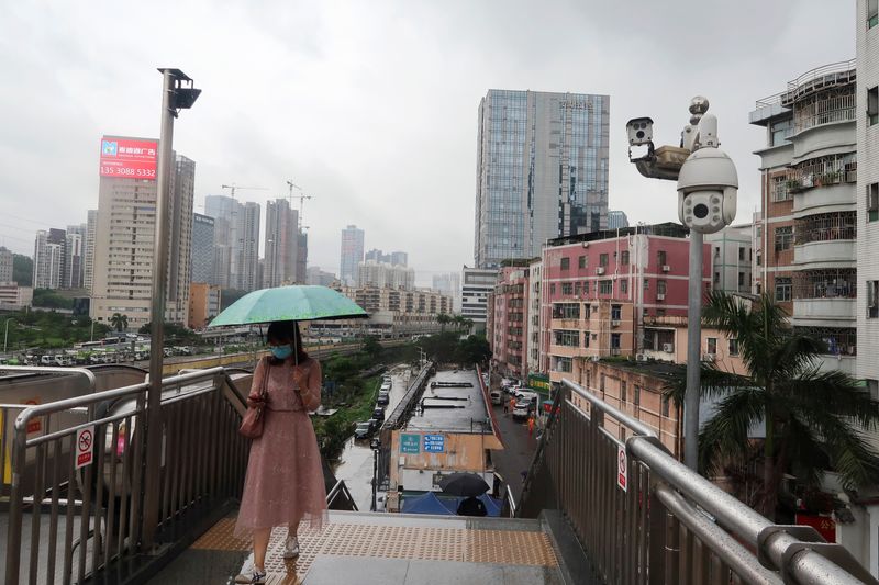 &copy; Reuters. Una mujer con un paraguas en la mano camina por un puente peatonal junto a cámaras de vigilancia, cerca de Caopu en el distrito Luohu de Shenzhen, provincia de Guangdong, China 5 de julio de 2022. REUTERS/David Kirton