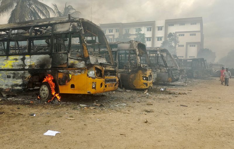 © Reuters. شخصان يسيران بجوار حافلات مدرسية محترقة في فناء مدرسة بمنطقة كالاكوريتشي بولاية تاميل نادو الهندية يوم الأحد. تصوير رويترز ( يحظر إعادة بيع الصورة أو وضعها في الأرشيف) . 
