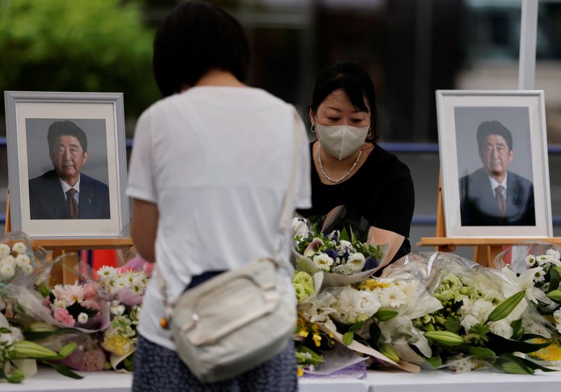 &copy; Reuters. A mourner offers flowers next to pictures of late former Japanese Prime Minister Shinzo Abe, who was shot while campaigning for a parliamentary election, on the day to mark a week after his assassination at the Liberal Democratic Party headquarters in Tok