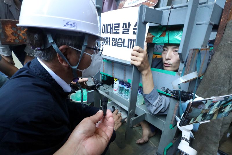 &copy; Reuters. South Korea's Employment and Labor Minister Lee Jung-sik talks with Yoo Choi-ahn, vice chief of the subcontractor union, who is locked inside a steel cage-like structure that he welded himself on the floor of the occupied oil tanker, during a strike at Da