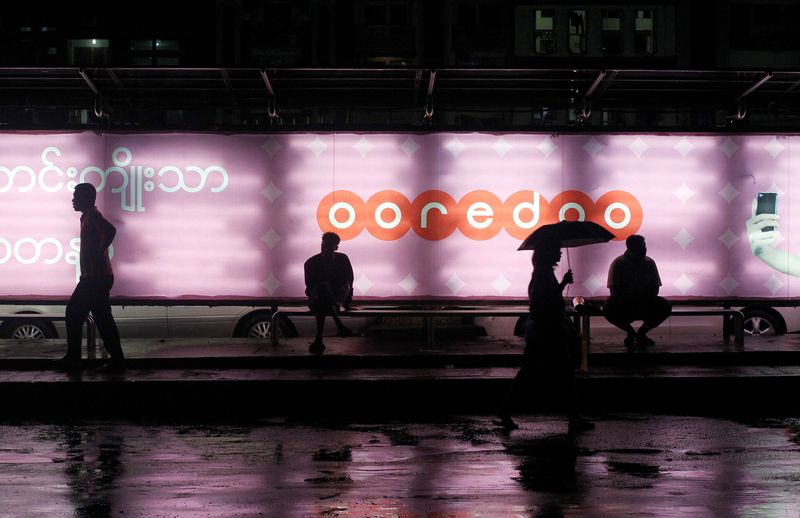 &copy; Reuters. FILE PHOTO: People sit at a bus station with an Ooredoo advertisement as they wait for a bus in Yangon, August 1, 2014. REUTERS/Soe Zeya Tun