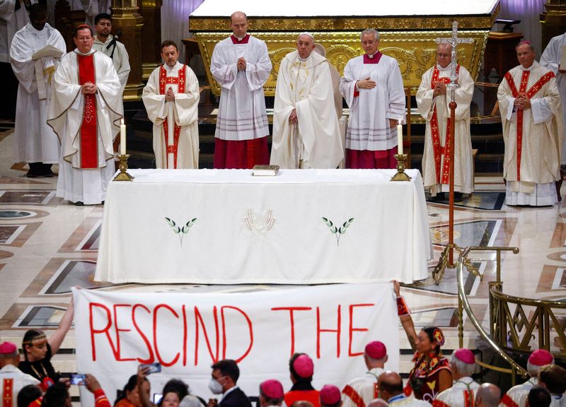 &copy; Reuters. People hold a banner as Pope Francis presides over a mass at the Shrine of Sainte-Anne-de-Beaupre, one of the oldest and most popular pilgrimage sites in North America, in Sainte-Anne-de-Beaupre, Quebec, Canada July 28, 2022. The banner reads: "Rescind th