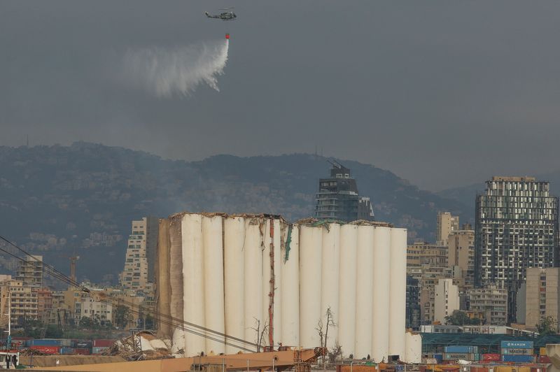 © Reuters. طائرة هليكوبتر ترش المياه على صوامع الحبوب المنهارة جزئيا في مرفأ بيروت يوم الأحد. تصوير محمد عزاقير- رويترز.