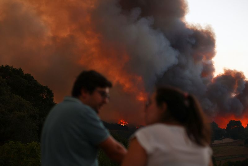 © Reuters. A couple looks at each other as smoke rises from a wildfire in Venda do Pinheiro in Mafra, Portugal, July 31, 2022. REUTERS/Pedro Nunes