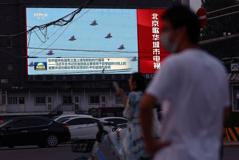 &copy; Reuters. Peatones esperan en una intersección cerca de una pantalla que muestra imágenes de aviones del Ejército Popular de Liberación chino (EPL) durante un programa de noticias nocturno, en Pekín, China, el 2 de agosto, 2022. REUTERS/Tingshu Wang