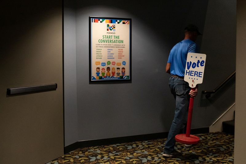 © Reuters. A city employee carries a 'Vote Here' sign to place outside the precinct the day before Michigan Democrats and Republicans choose their nominees to contest November's congressional elections, which will determine which party controls U.S. House of Representatives for next two years, in Birmingham, Michigan, U.S. August 1, 2022.  REUTERS/Emily Elconin