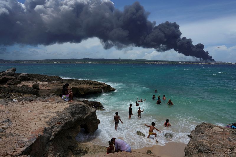&copy; Reuters. People enjoy the beach near the smoke of a fire over fuel storage tanks that exploded near Cuba's supertanker port in Matanzas, Cuba, August 6, 2022. REUTERS/Alexandre Meneghini