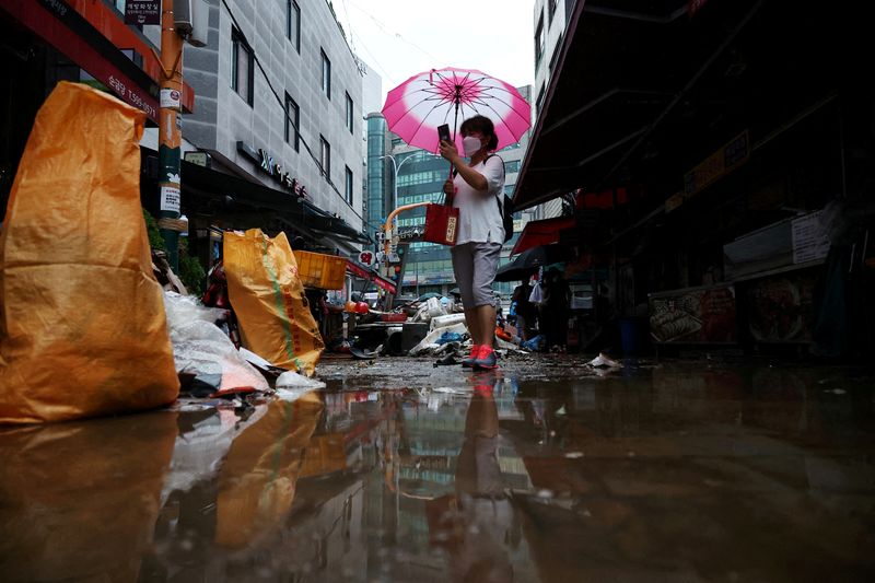 &copy; Reuters. A woman using an umbrella takes photographs of a road that was flooded after torrential rain, at a traditional market in Seoul, South Korea, August 9, 2022.   REUTERS/Kim Hong-Ji     