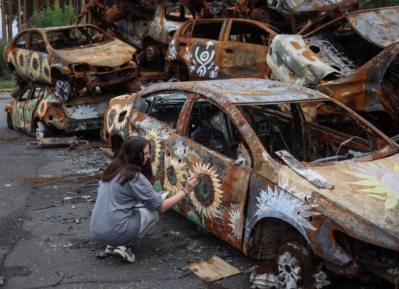 &copy; Reuters. Ukrainian artist Olena Yanko paints a car destroyed during Russia's attack on Ukraine and then collected from different places in the town of Irpin in Kyiv region, Ukraine August 10, 2022. REUTERS/Gleb Garanich