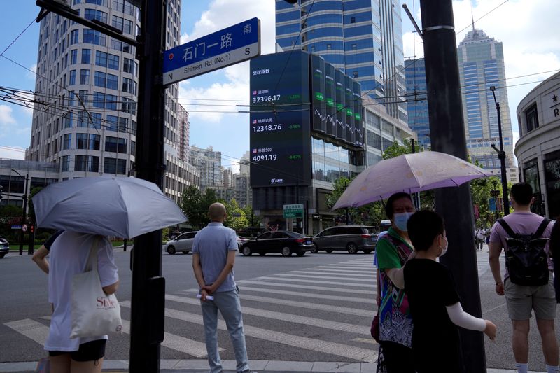 © Reuters. Pedestrians wait to cross a road at a junction near a giant display of stock indexes in Shanghai, China August 3, 2022. REUTERS/Aly Song/File Photo