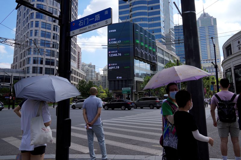 &copy; Reuters. Imagen de archivo de peatones esperando para cruzar una calle en una esquina cerca de una pantalla gigante que muestra índices bursátiles en Shanghái, China. 3 de agosto, 2022. REUTERS/Aly Song/Archivo