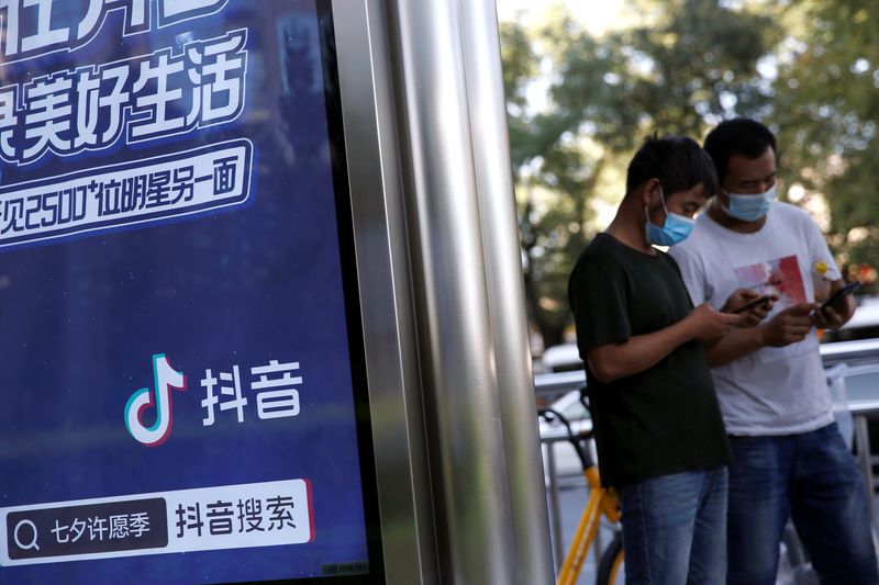 &copy; Reuters. People wearing face masks following the coronavirus disease (COVID-19) outbreak use smartphones next to an advertisement of TikTok (Douyin) at a bus stop in Beijing, China August 24, 2020. REUTERS/Tingshu Wang