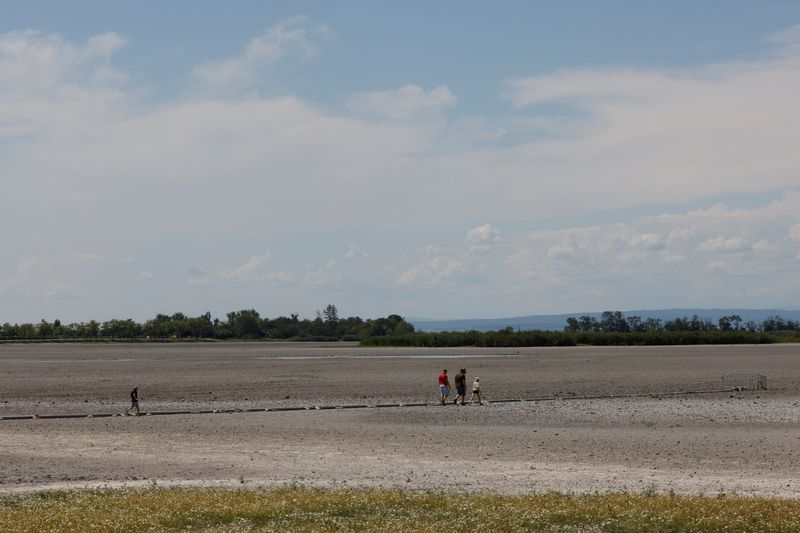 &copy; Reuters. FILE PHOTO: People walk in almost dried up Lake Zicksee near Sankt Andrae, as another heatwave is predicted for parts of the country, in Austria, August 12, 2022. REUTERS/Leonhard Foeger