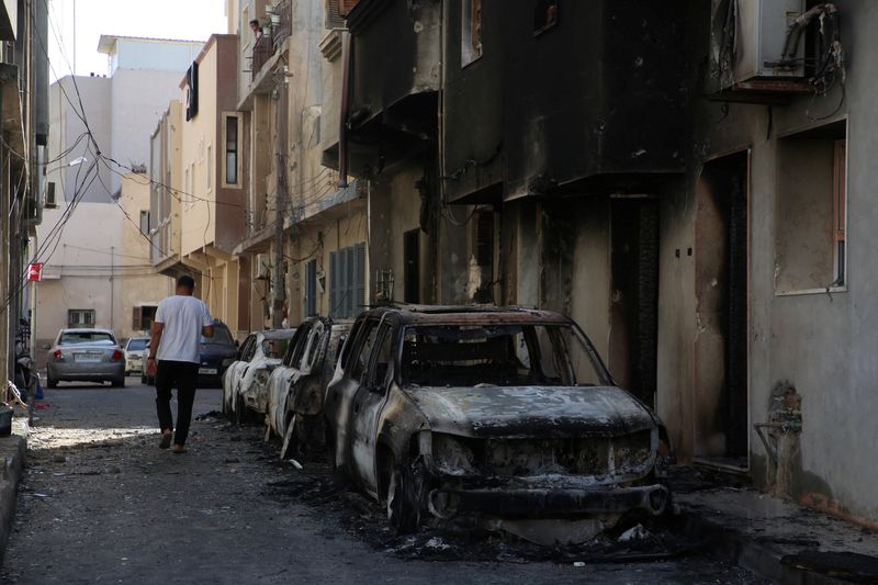 &copy; Reuters. رجل يسير إلى جانب سيارات متفحمة بعد يوم من اشتباكات شهدتها طرابلس في ليبيا يوم السبت. تصوير: حازم أحمد - رويترز