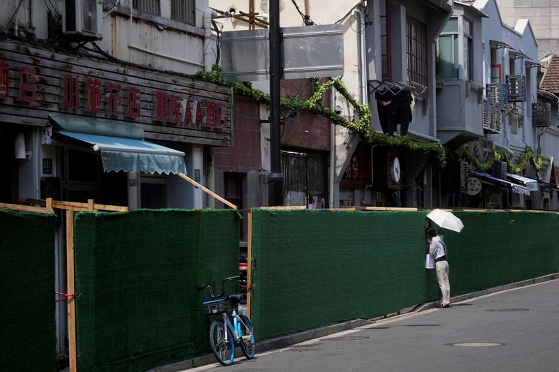 &copy; Reuters. FILE PHOTO: A woman looks in through a gap in a barrier at a residential area, amid new lockdown measures in parts of the city to curb the coronavirus disease (COVID-19) outbreak in Shanghai, China July 11, 2022. REUTERS/Aly Song