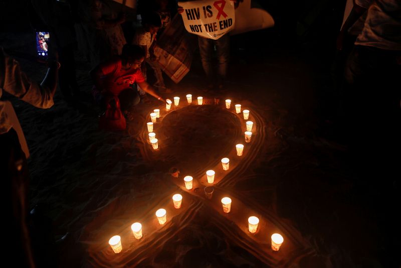 &copy; Reuters. FILE PHOTO: A woman arranges candles in the formation of a ribbon, the symbol for the solidarity of people living with AIDS on World AIDS Day on a beach in Mumbai, India, December 1, 2019. REUTERS/Francis Mascarenhas