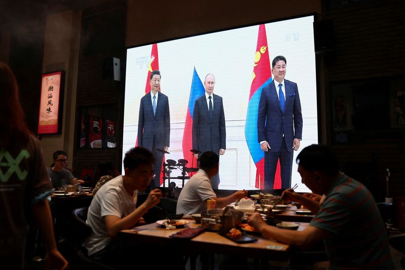 &copy; Reuters. Clientes cenan cerca de una pantalla gigante que emite imágenes de noticias del presidente chino, Xi Jinping, el presidente ruso, Vladimir Putin, y el presidente mongol, Ukhnaa Khurelsukh, posando para una foto durante una reunión al margen de la cumbre
