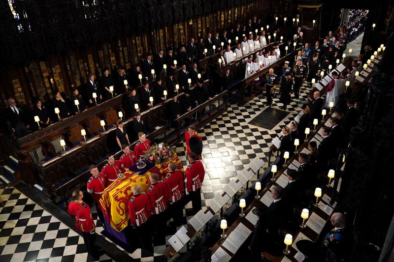 © Reuters. The coffin of Queen Elizabeth II, followed by (left to right, from front) King Charles III, the Queen Consort, the Princess Royal, Vice Admiral Sir Tim Laurence, the Duke of York, the Earl of Wessex, the Countess of Wessex, the Prince of Wales, Prince George, Princess Charlotte, the Princess of Wales, the Duke of Sussex, the Duchess of Sussex, Peter Phillips, the Earl of Snowdon, the Duke of Gloucester, the Duke of Kent, and Prince Michael of Kent,  is carried by the Bearer Party in to the Committal Service at St George's Chapel in Windsor Castle, Berkshire. Picture date: Monday September 19, 2022. Victoria Jones/Pool via REUTERS