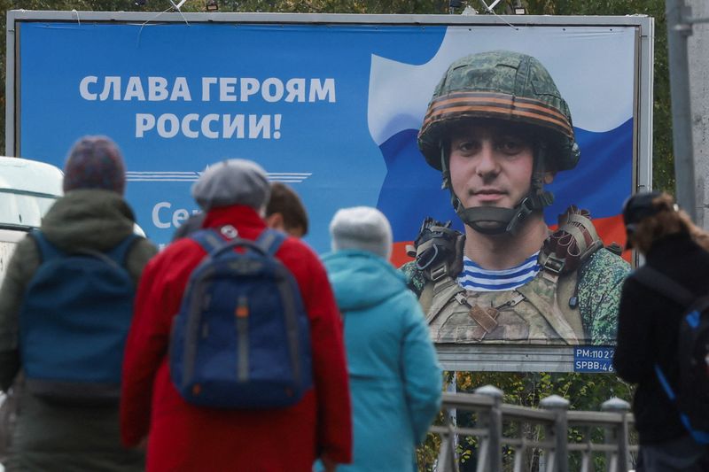 &copy; Reuters. Persone ad una fermata del tram a San Pietroburgo, di fronte ad un cartello con scritto "Viva gli eroi della Russia". 21 settembre 2022.   REUTERS/Anton Vaganov
