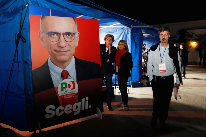 &copy; Reuters. أشخاص يقفون بجانب ملصق يحمل صورة إنريكو ليتا أمين عام الحزب الديمقراطي الذي يمثل يسار الوسط بإيطاليا يوم الأحد. تصوير : ريمو كاسيللي- رويترز 
