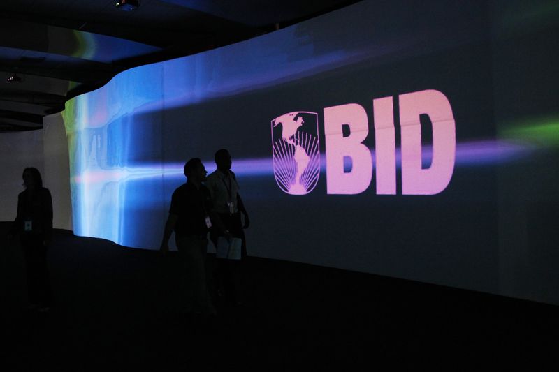 © Reuters. Visitors walk past a screen with the logo of Banco Interamericano de Desarrollo (BID) at the Atlapa Convention Center in Panama City March 13, 2013. REUTERS/Carlos Jasso 