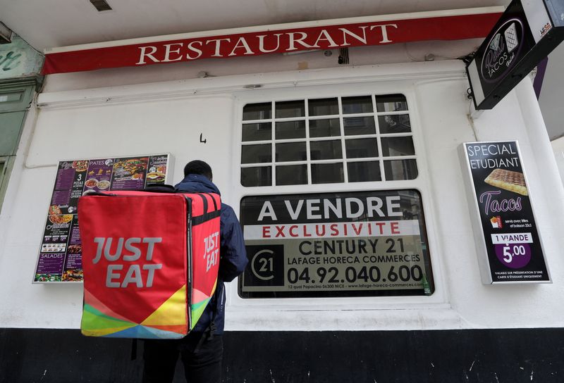 © Reuters. FILE PHOTO: A Just Eat delivery man stands in front of a closed restaurant on sale in Nice amid the coronavirus disease (COVID-19) outbreak in France, February 16, 2021.   REUTERS/Eric Gaillard/File Photo