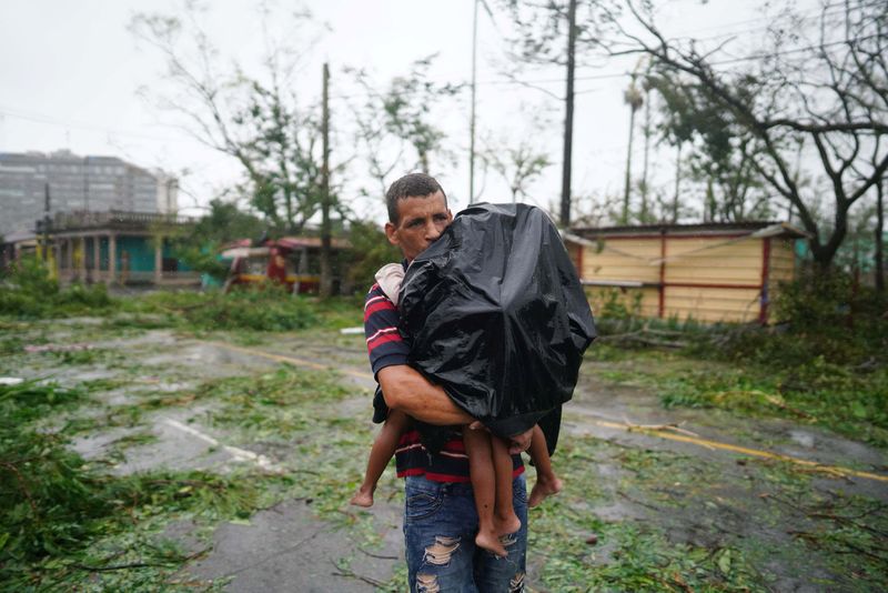 © Reuters. A man carries his children next to debris caused by the Hurricane Ian after it passed in Pinar del Rio, Cuba, September 27, 2022. REUTERS/Alexandre Meneghini