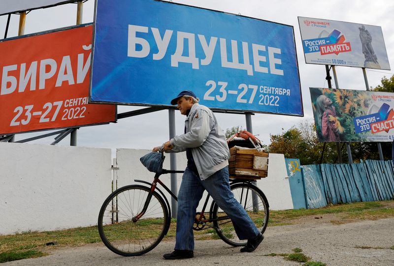 &copy; Reuters. Um homem passa com sua bicicleta diante de placas que anunciam o referendo pela anexação russa na cidade de Melitopol, na região de Zaporizhzhia. 27 setembro, 2022. REUTERS/Alexander Ermochenko   