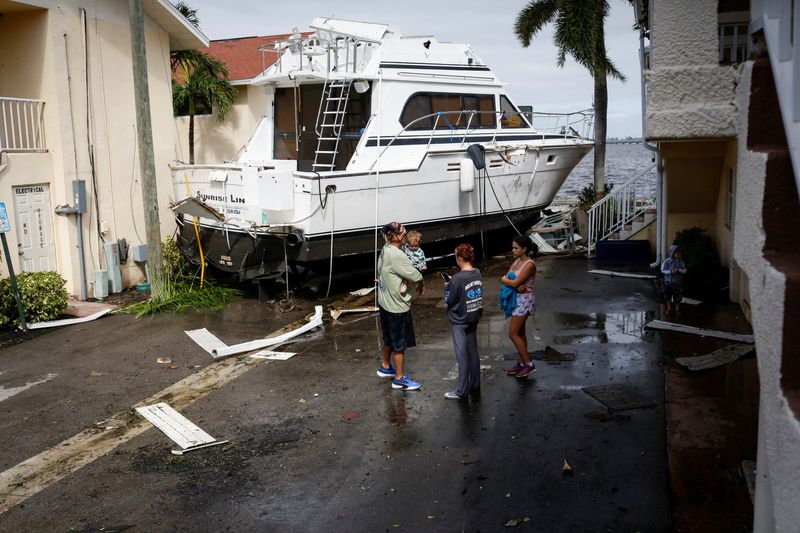 © Reuters. A family stands next to a damaged boat amid a downtown condominium after Hurricane Ian caused widespread destruction in Fort Myers, Florida, U.S., September 29, 2022. REUTERS/Marco Bello