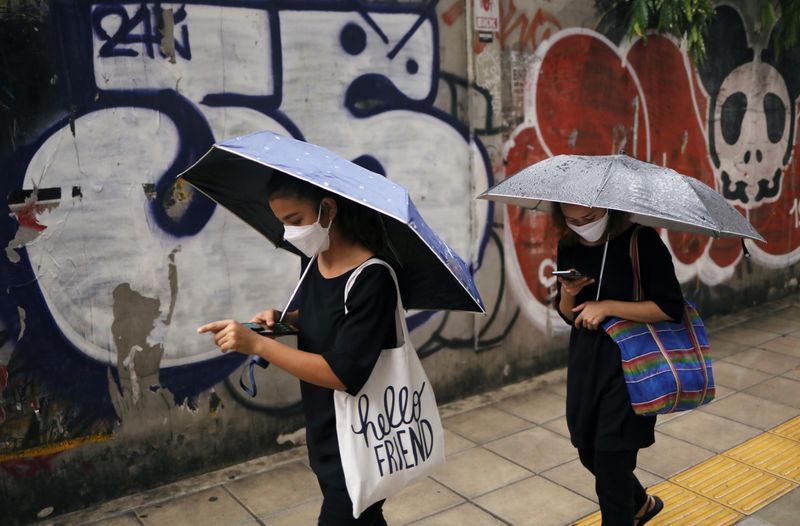 © Reuters. Pedestrians wearing protective masks use their mobile phones as they hold umbrellas during rainy weather, after the government eased some protective measures following the coronavirus disease (COVID-19) outbreak in Bangkok, Thailand June 17, 2020. REUTERS/Jorge Silva