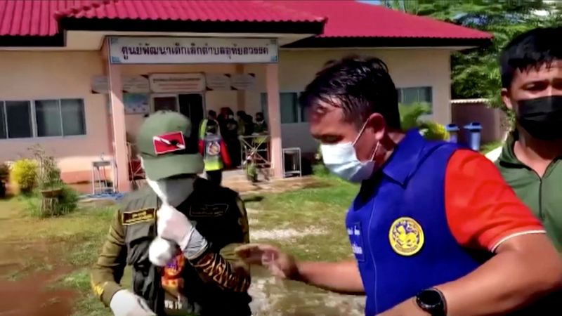 © Reuters. １０月６日、タイ警察によると、北東部の託児施設で男が銃を乱射し、３４人が死亡した。写真は乱射が発生したタイ北東部のUthai Sawanの託児施設の入り口を封鎖する当局者ら。提供動画より（２０２２年　ロイター/TPBS）