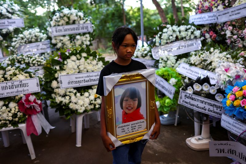 © Reuters. A girl holds up a picture of her younger sister, at a mass funeral at Wat Si Uthai temple, following a mass shooting in the town of Uthai Sawan in the province of Nong Bua Lam Phu, Thailand, October 8, 2022. REUTERS/Athit Perawongmetha