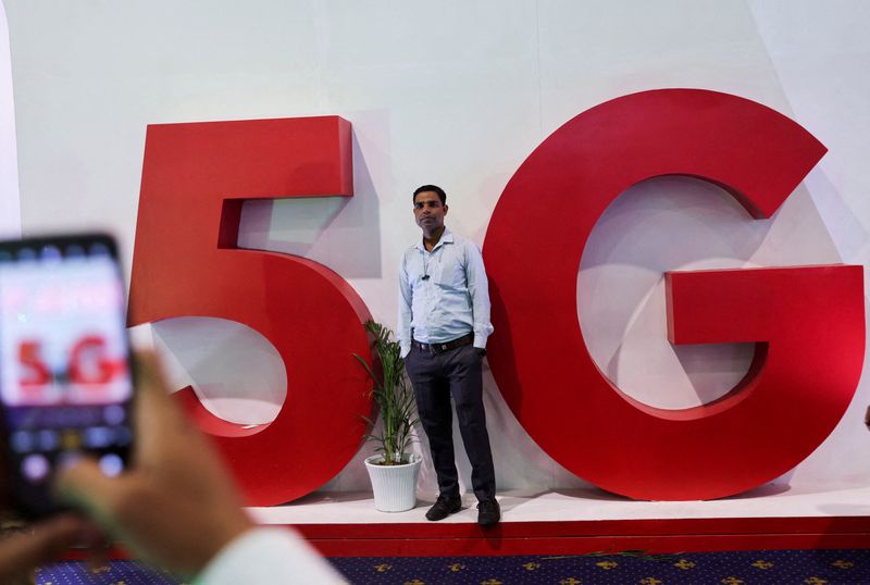 © Reuters. FILE PHOTO: A man takes a picture of a friend in front of a sign showing installation of the 5G network in New Delhi, India, October 3, 2022. REUTERS/Anushree Fadnavis/File Photo