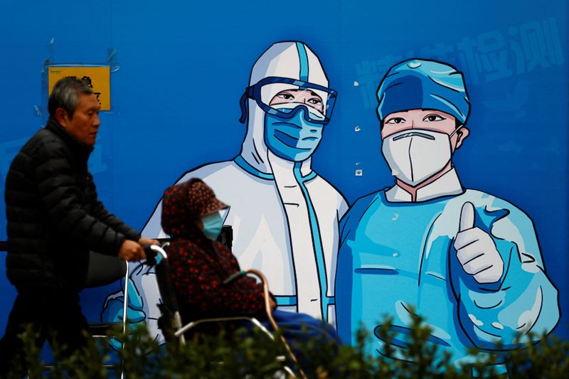 &copy; Reuters. FILE PHOTO: A man pushes a woman in wheelchair past a poster with a graphic of medical workers at a nucleic acid testing booth for the coronavirus disease (COVID-19) , in Beijing, China October 27, 2022. REUTERS/Tingshu Wang