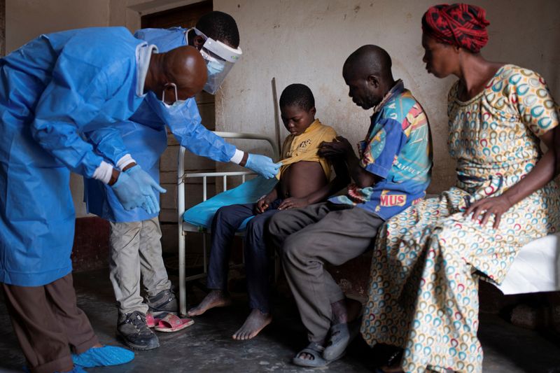 © Reuters. Marcel Osekasomba, 48, head nurse at the Yalolia health centre, and Theopiste Maloko, 42, a local health official, check the progress of Lisungi Lifafu, 12, who is suffering from monkeypox, while his father Litumbe Lifafu and mother, Lituka Yenga, watch, in Yalolia village, Yakusu, Tshopo, Democratic Republic of Congo, October 3, 2022. Without treatment Lisungi can only wait for the illness to run its course. Ahead of him lies a myriad of possible outcomes including recovery, blindness, or, as was the case with a family member in August, death. 