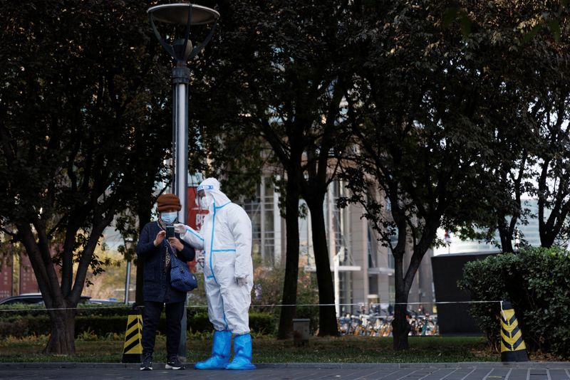 &copy; Reuters. A pandemic prevention worker wears a protective suit as he checks personal details of a woman lining up to get a swab test at a testing booth as outbreaks of coronavirus disease (COVID-19) continue in Beijing, China, November 3, 2022. REUTERS/Thomas Peter