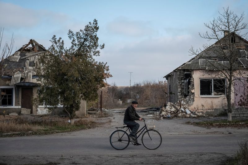 &copy; Reuters. أحد السكان يقود دراجة قرب منازل مدمرة في قرية في منطقة خيرسون الأوكرانية يوم الثلاثاء. صورة لرويترز.