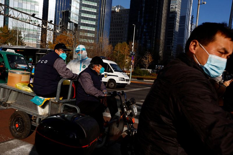 &copy; Reuters. Personale con tuta protettiva viaggia su un triciclo elettrico durante l'ora di punta mattutina, in seguito al diffondersi dell'epidemia di coronavirus (Covid-19), nel Central Business District (CBD) nel distretto di Chaoyang, Pechino, Cina 21 novembre 20