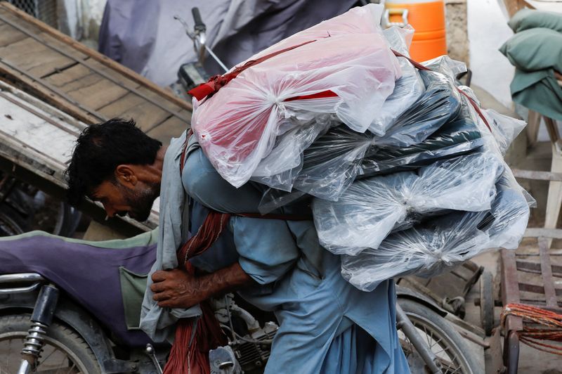 © Reuters. A labourer bends over as he carries packs of textile fabric on his back to deliver to a nearby shop in a market in Karachi, Pakistan June 24, 2022. REUTERS/Akhtar Soomro