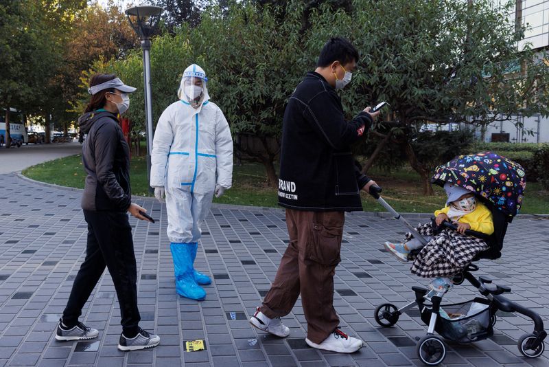 &copy; Reuters. Un addetto alla prevenzione della pandemia con una tuta protettiva di fronte a delle persone in fila per sottoporsi a test con tampone, mentre continuano i focolai di malattia da coronavirus (COVID-19) a Pechino, Cina, 3 novembre 2022. REUTERS/Thomas Pete