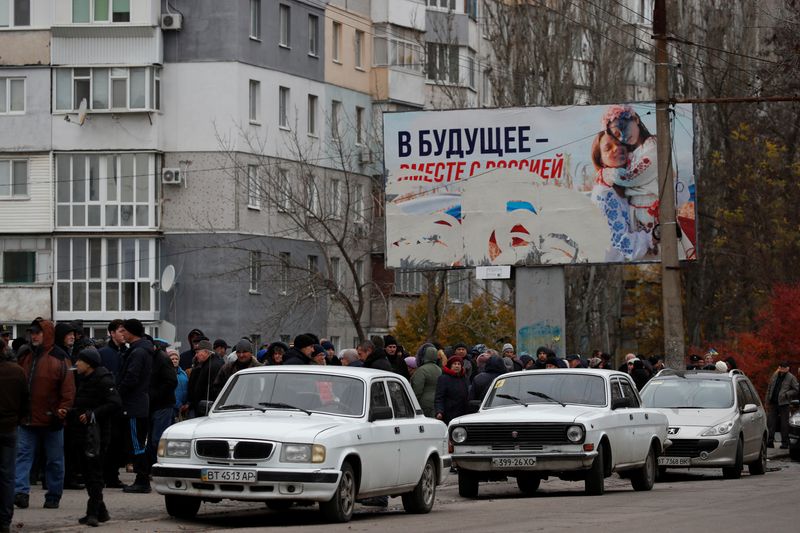 &copy; Reuters. Des personnes attendent la distribution d'aide humanitaire, avec un panneau publicitaire pro-russe en arrière-plan, après la retraite militaire de la Russie de Kherson, en Ukraine. /Photo prise le 22 novembre 2022/REUTERS/Murad Sezer