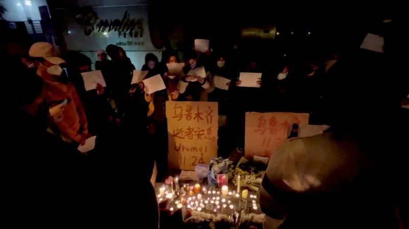 &copy; Reuters. People hold signs and light candles during a vigil held for the victims of the Urumqi fire, in Shanghai, China November 26, 2022 in this picture obtained from a social media video. Gao Ming/via REUTERS  