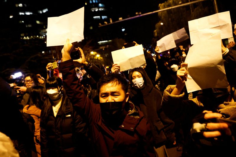 &copy; Reuters. Un grupo de personas se reúne para una vigilia y sostiene hojas de papel blancas en protesta por las restricciones a la enfermedad del coronavirus (COVID-19), en un acto de conmemoración de las víctimas de un incendio en Urumqi, mientras continúan los