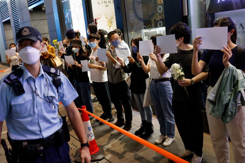 © Reuters. People hold white sheets of paper and flowers in a row as police check their IDs during a protest over coronavirus disease (COVID-19) restrictions in mainland China, during a commemoration of the victims of a fire in Urumqi, in Hong Kong, China November 28, 2022. REUTERS/Tyrone Siu