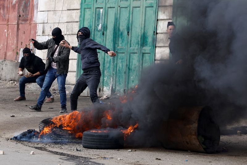 &copy; Reuters. إطارات سيارات تشتعل فيها النيران بينما يرشق محتجون فلسطينيون القوات الإسرائيلية بالحجارة أثناء اشتباكات بين الجانبين بالقرب من الخليل في 