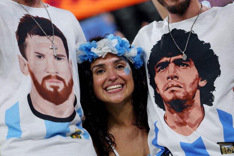 &copy; Reuters. Torcedora da Argentina junto a torcedores com camisas com as imagens de Lionel Messi e Diego Maradona antes de partida contra a Polônia na Copa do Mundo do Catar
30/11/2022 REUTERS/Amanda Perobelli