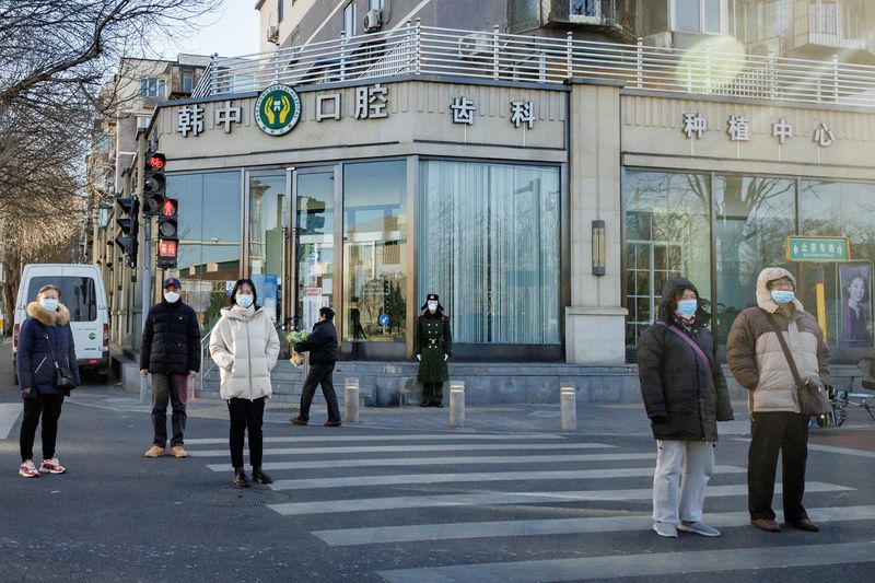 &copy; Reuters. أحد أفراد الجيش الصيني يضع كمامة على وجهه بينما يقف أشخاص آخرون في شارع بالعاصمة بكين وهم يضعون الكمامات في  الأول من ديسمبر كانون الأول 2022 و