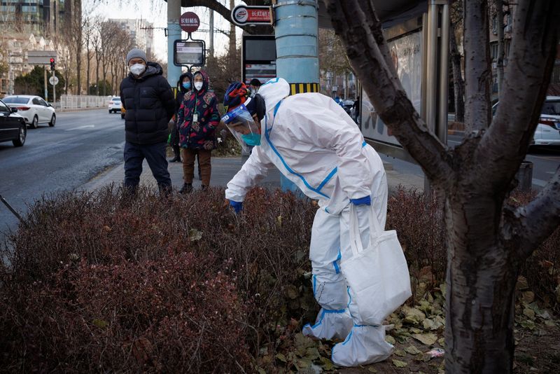 © Reuters. A street cleaner wears a protective suit as she picks up litter next to a bus stop as coronavirus disease (COVID-19) outbreaks continue in Beijing, December 7, 2022. REUTERS/Thomas Peter