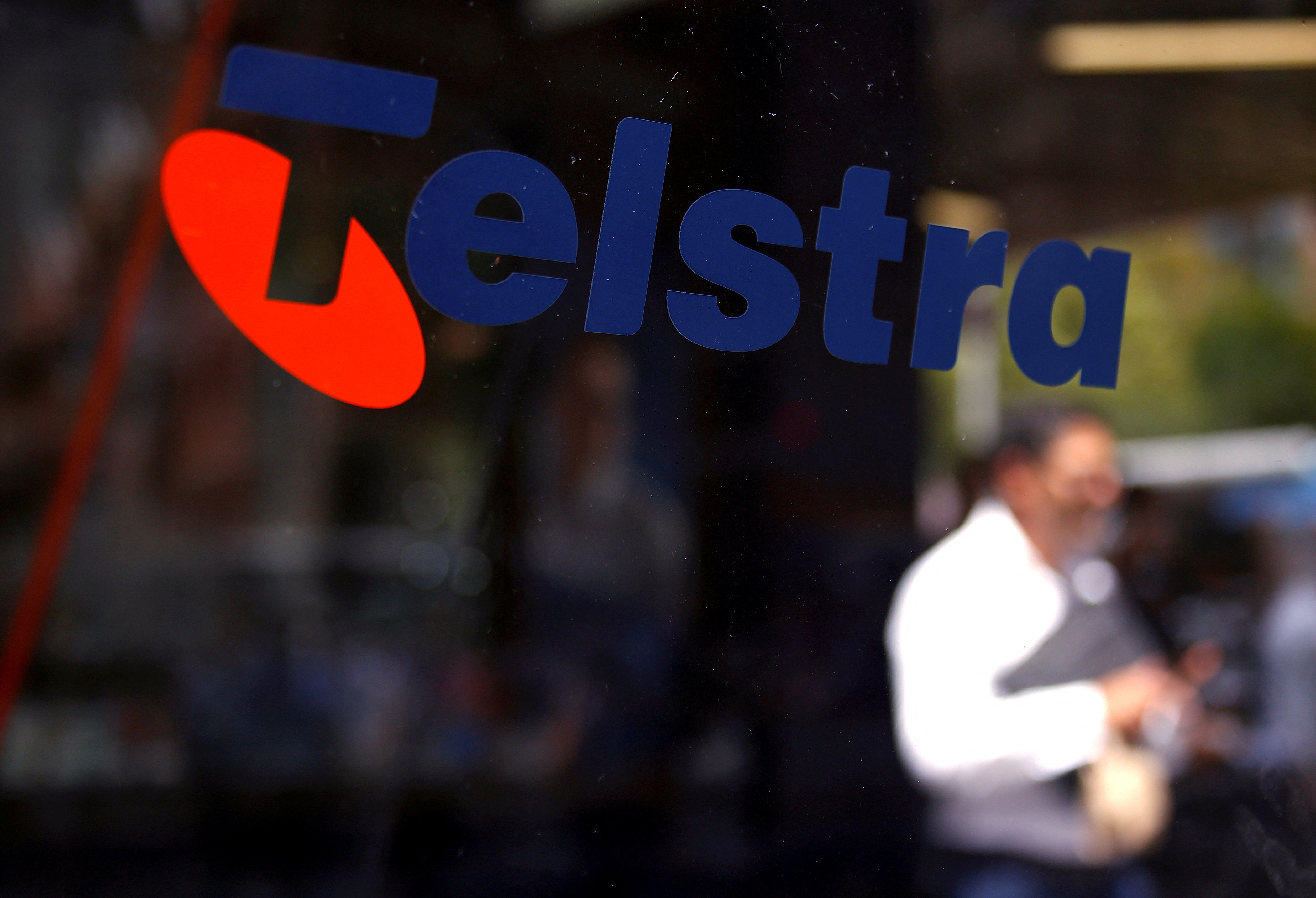 &copy; Reuters. FILE PHOTO: A man looks at his phone as he walks past a Telstra logo adorning a phone booth in the central business district (CBD) of Sydney in Australia, February 13, 2018.  REUTERS/David Gray